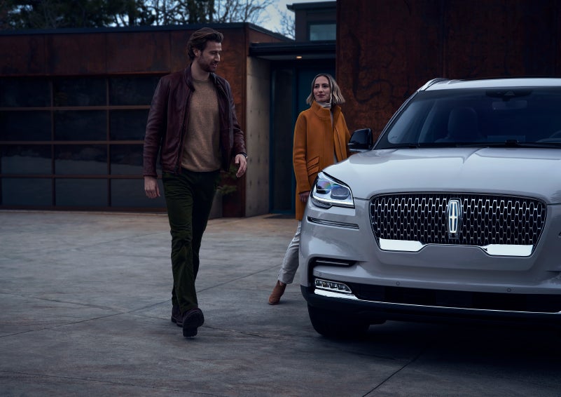 A man and a woman approaching a 2024 Lincoln Aviator® SUV, which illuminates certain lights when they are close | Lincoln Demo 5 in Derwood MD